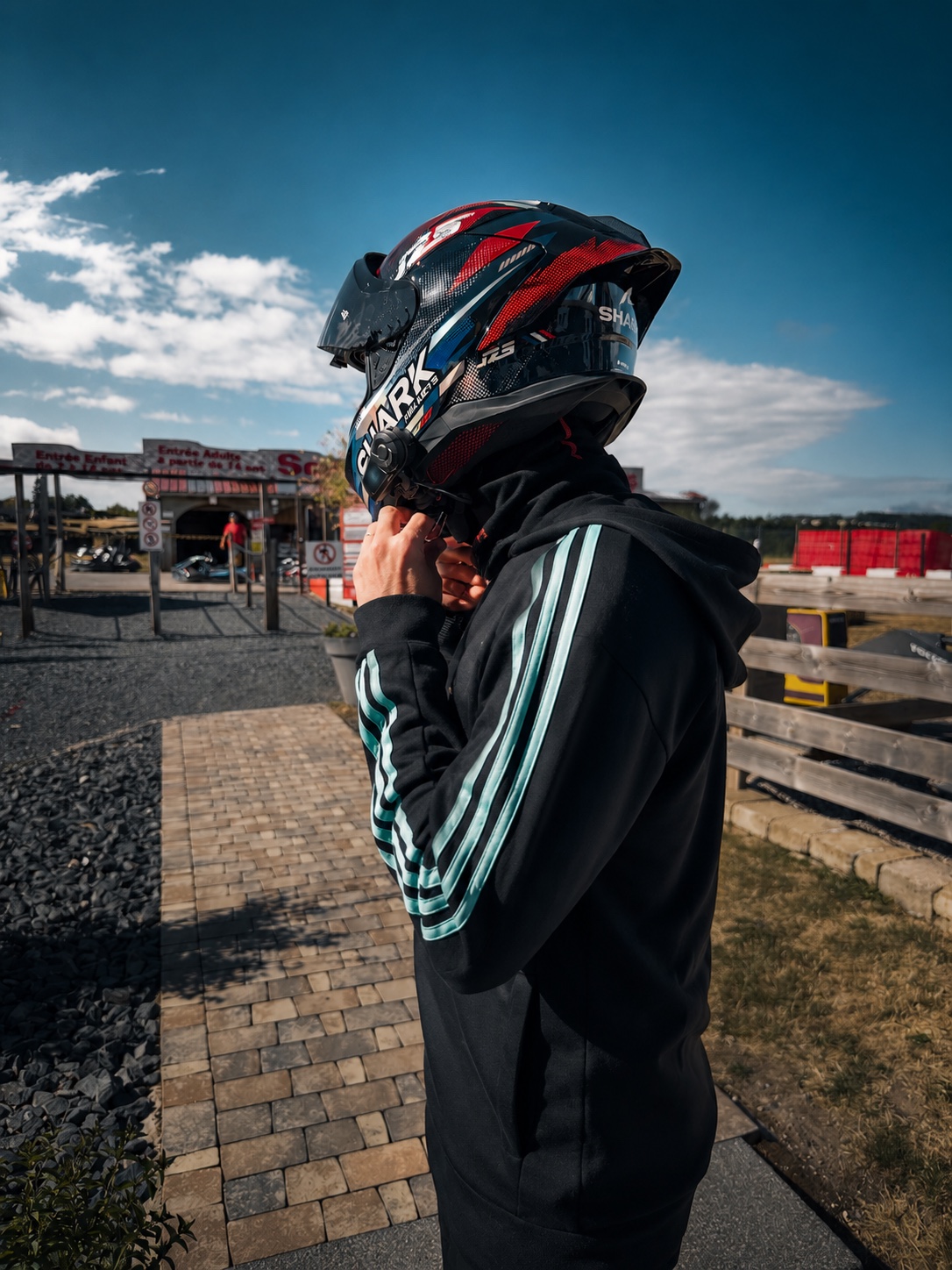 Pilote ajustant la jugulaire de son casque intégral à l'entrée d'un circuit de karting outdoor
