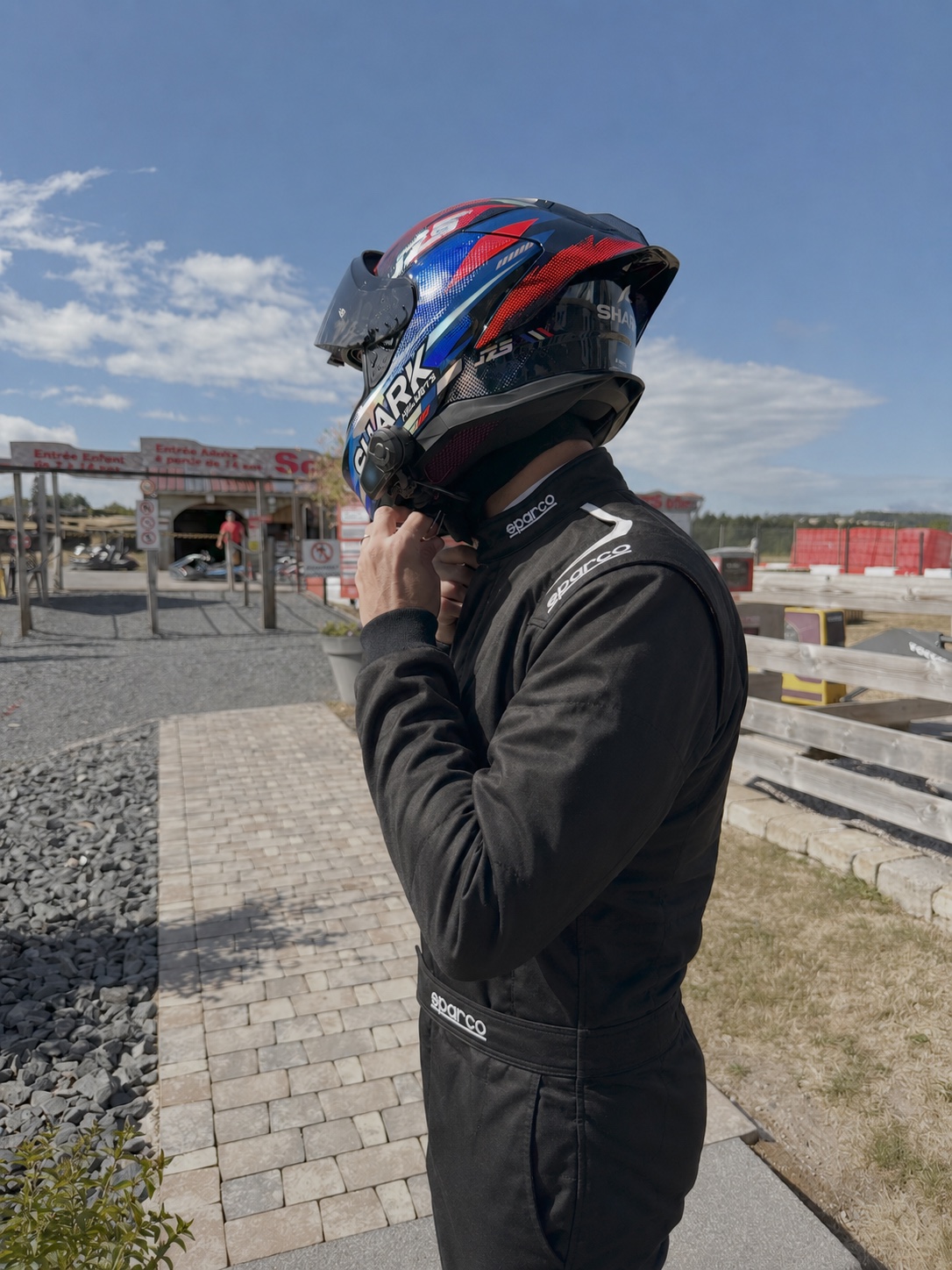 Pilote en combinaison Sparco ajustant son casque avant de rejoindre la piste, circuit de karting outdoor